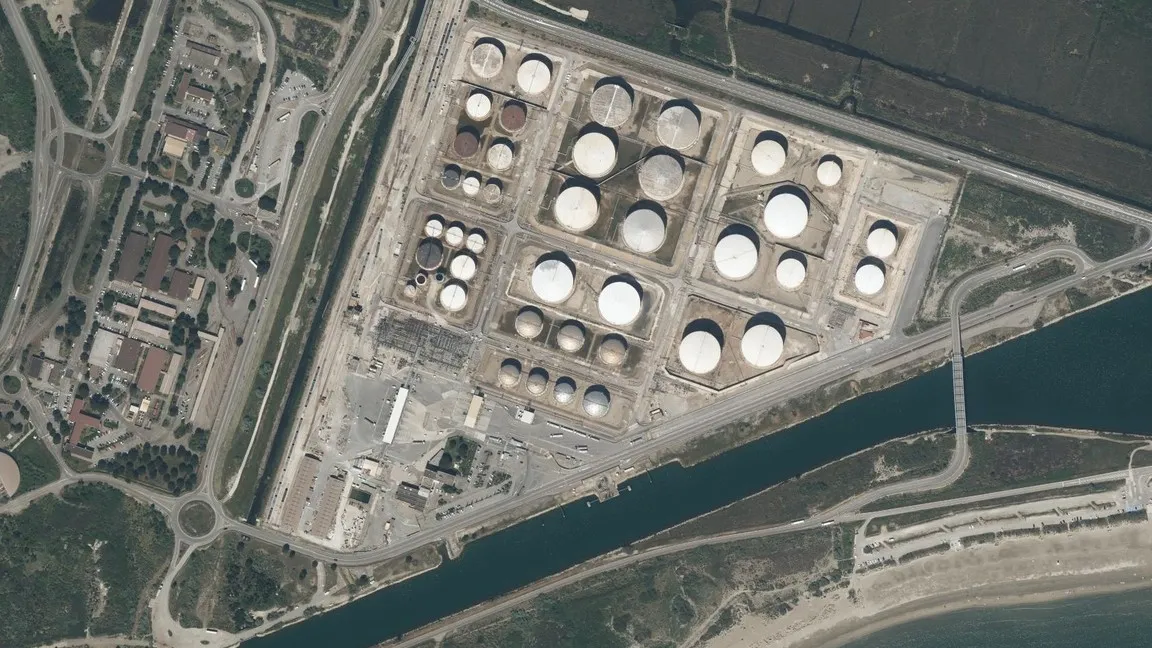 Vue aérienne d’un dépôt pétrolier portuaire : rangées de cuves, un navire à quai et des conteneurs