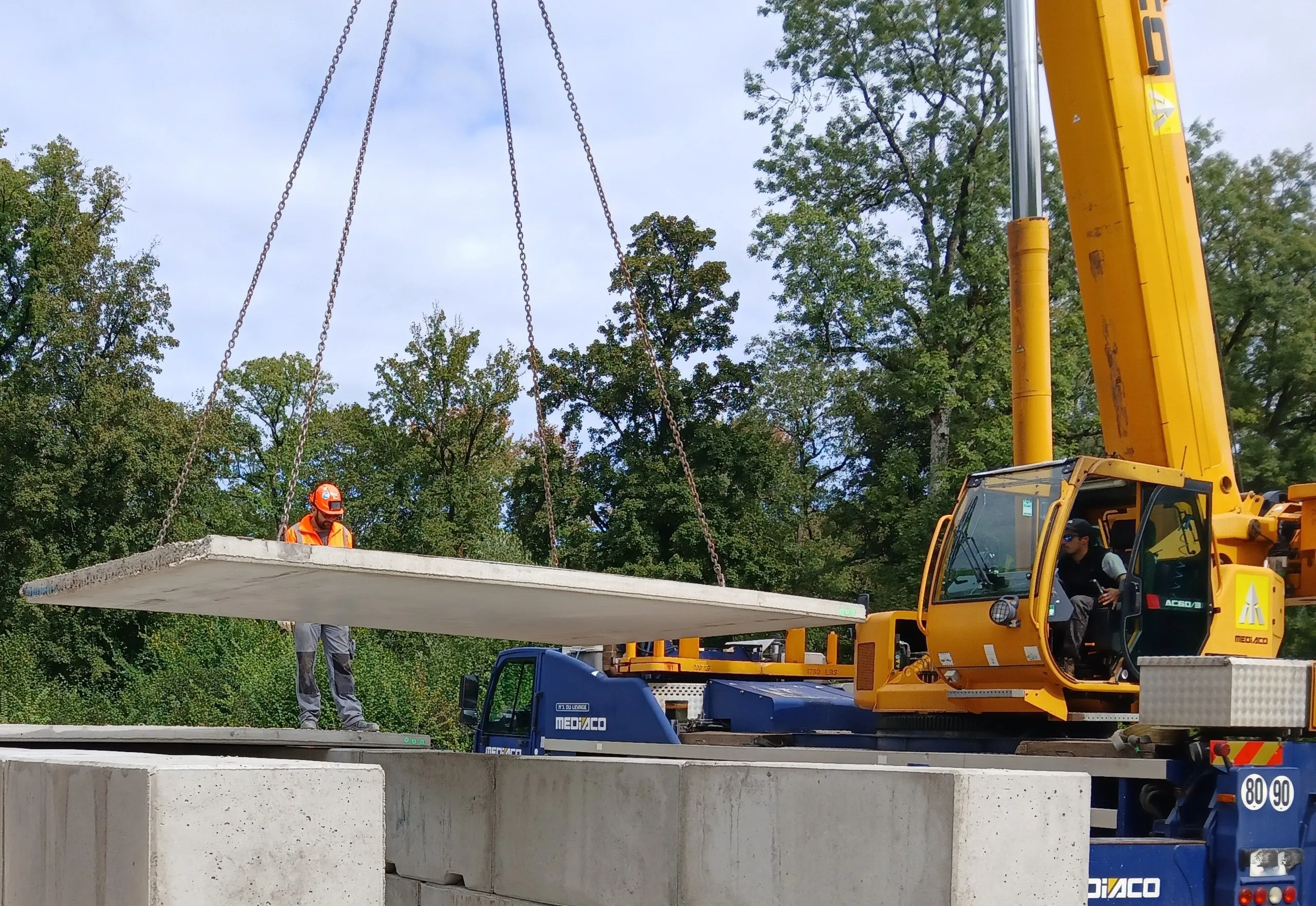 Grue mobile posant une dalle de béton sur un mur de blocs, lors de l’aménagement du champ de tir